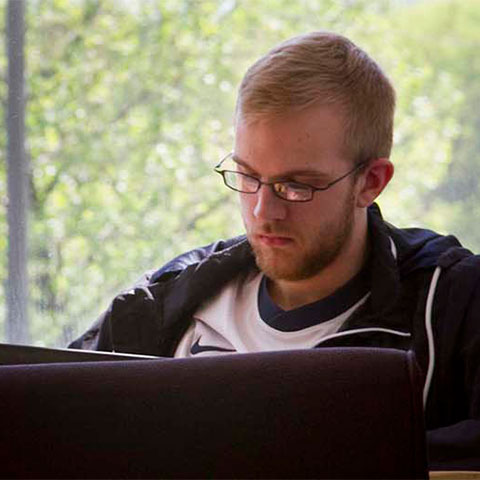 Student sits in common area working on laptop
