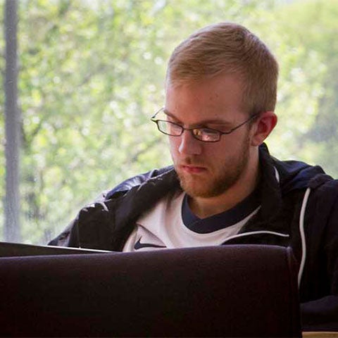 Student sits in common area working on laptop