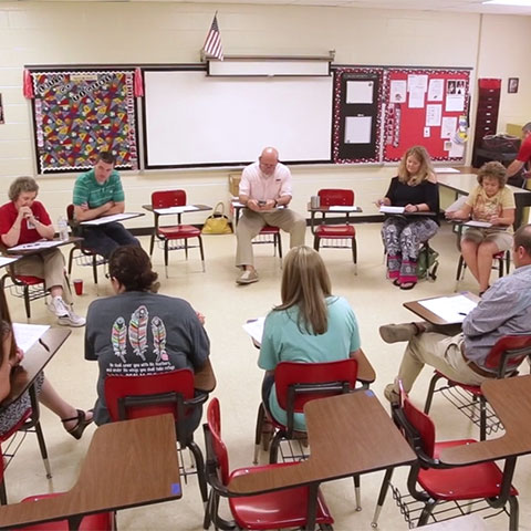 Teachers sit in desks in a circle during professional learning.