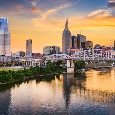 Nashville skyline at dusk with Cumberland river in the foreground.