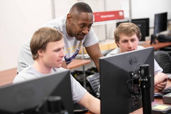 students working together on the computer while the teacher leans over their shoulders to help