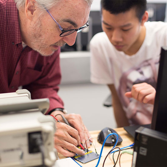 Engineering professor assists student with soldering during a electrical lab