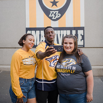 Three students take a selfie in front of the Smashville mural