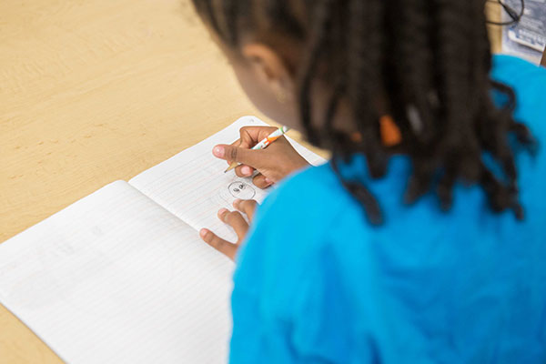 A child draws an image in a composition notebook