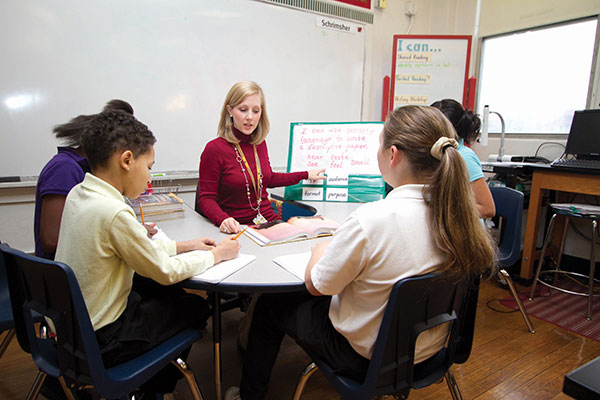 A teacher sits across from four students instructing them on how to write well