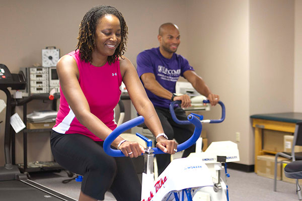 A woman and a man ride exercise bikes in a fitness room