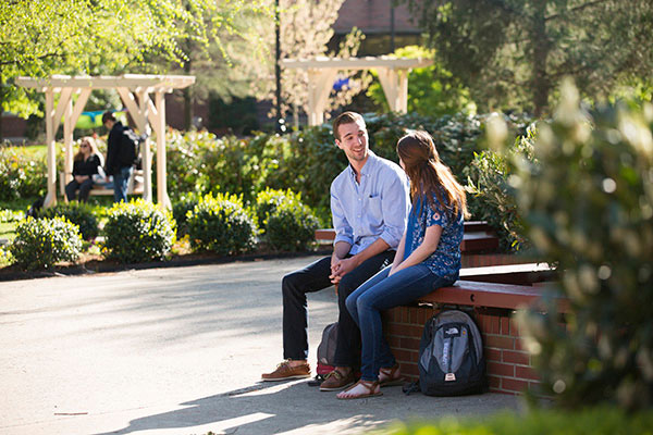 Two students sit outside on a bench talking