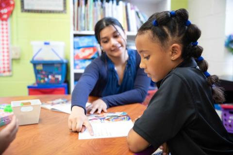 Teacher sitting at desk with students reading. 