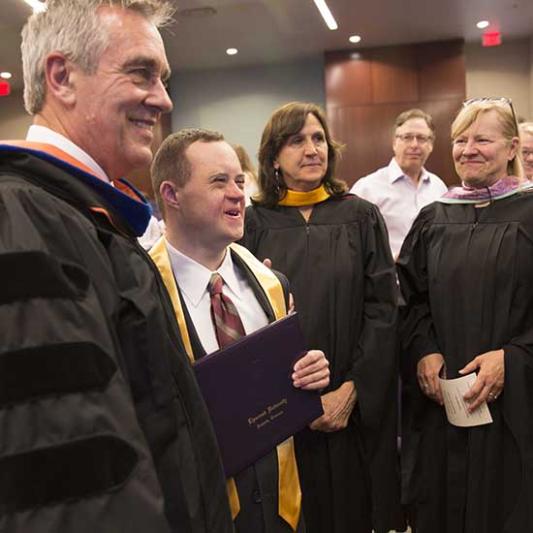 IDEAL students stand beside their professors in graduation robes.