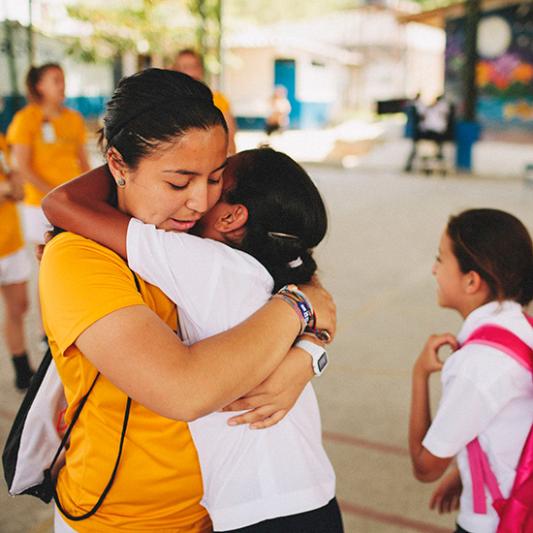 A Lipscomb student on mission and a young student hug in El Salvador. 