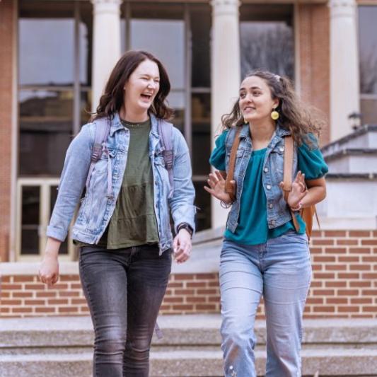 Two girls laughing and walking across campus