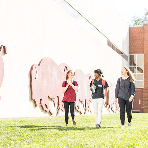 Students walk outside Student Activities Center near mural of running bison.