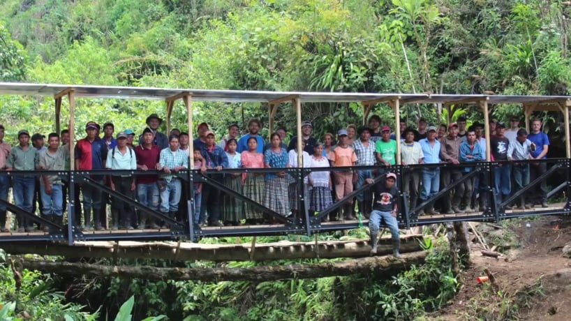 Locals and student engineering team take a photo on a bridge built as an Engineering Mission project