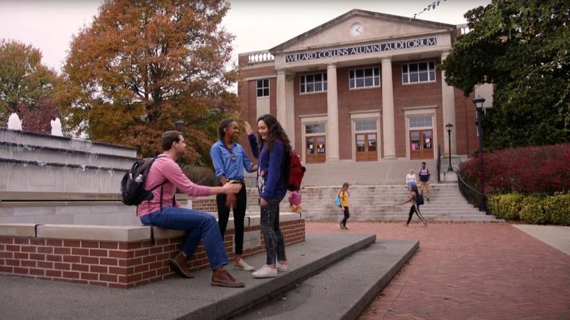 Three students talking next to the fountain on campus.