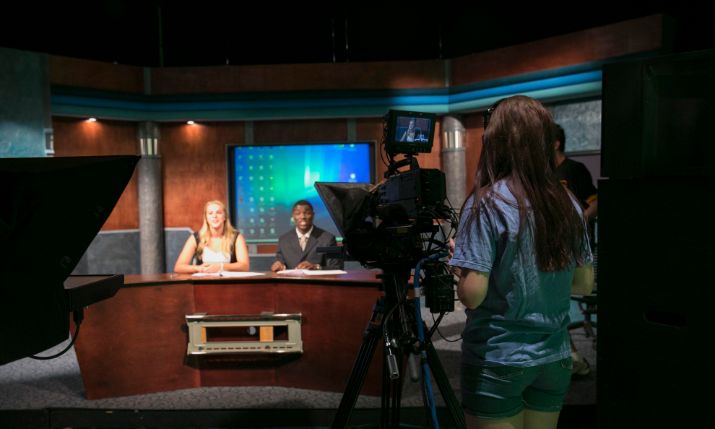 Student operating camera in news studio.