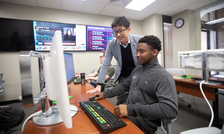 Student working in the computer lab with a professor.