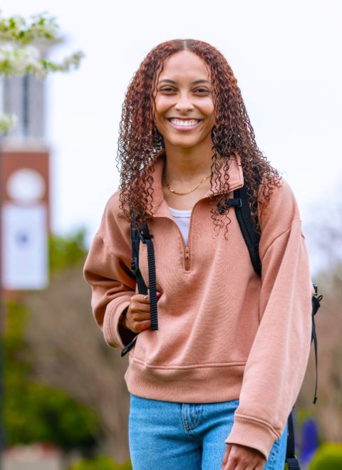 Student standing and smiling in front of the bell tower in spring