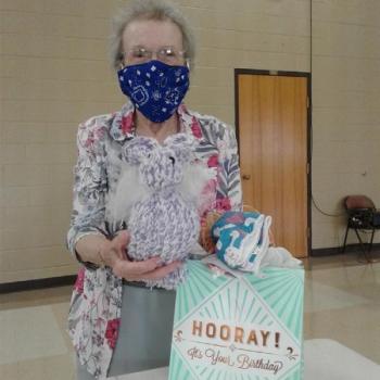 Woman wearing face mask holding packaged meal.