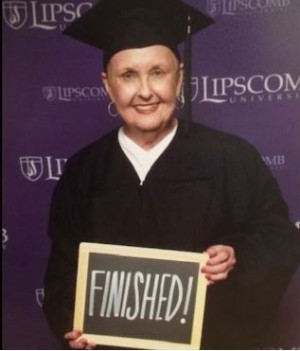Linda Rhine in cap and gown holding a finished sign