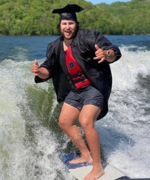 Grant Mitchell surfing in a graduation cap and gown