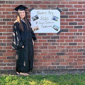 Noelle Lusk in cap and gown with a celebration sign