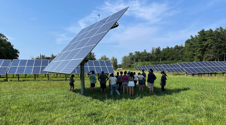 Students get some shade under a gigantic solar panel on a bright summer day.