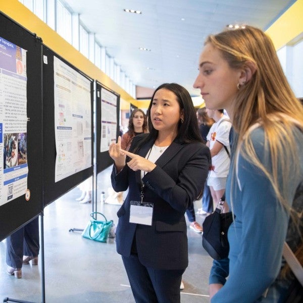 Kaylee Grace Wu standing at poster presentation and engaging with student observer