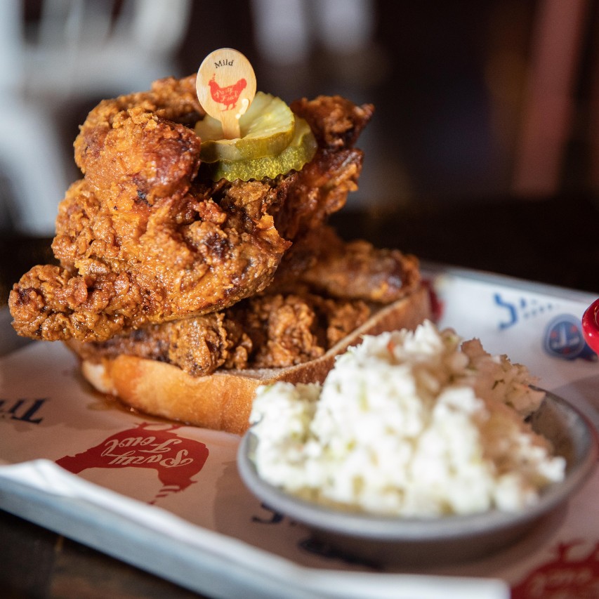 half of a fried chicken cut into two pieces on bread served on a plate with slaw