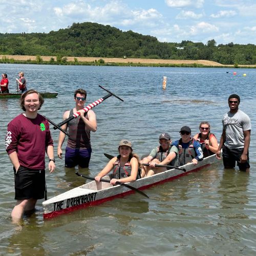 students posing in the water with a canoe at the concrete canoe competition
