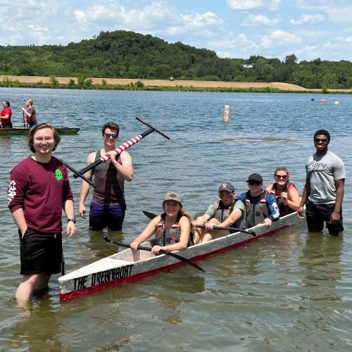 students posing in the water with a canoe at the concrete canoe competition