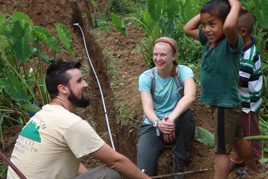 A male and female student kneeling interact with local children from Setzimaaj, Guatemala