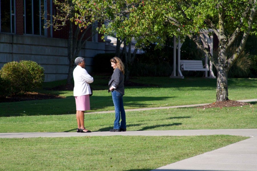 Norma Burgess standing outside on a sidewalk talking to a student on campus.