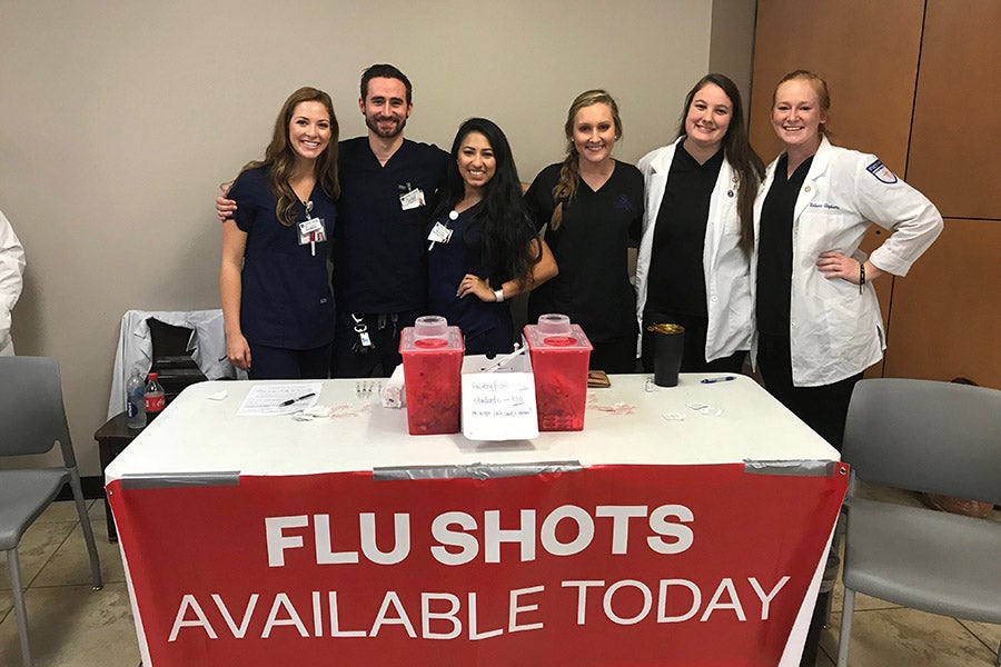 Student pharmacists gathered behind a flu shot booth with banner