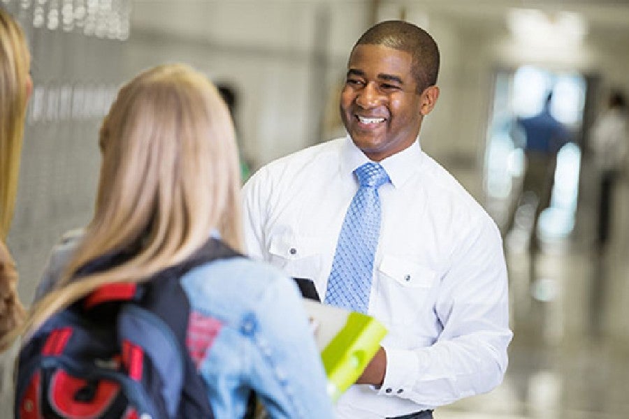 Educator standing in school hallway talking to teacher