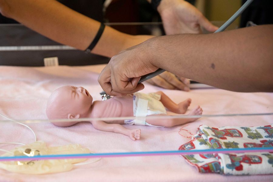 Students practice listening to heartbeat on infant medical dummy 
