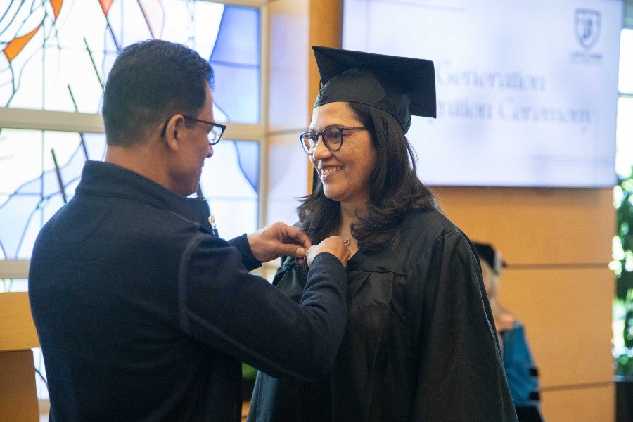 A husband pinning his wife, a May 2023 first generation graduate