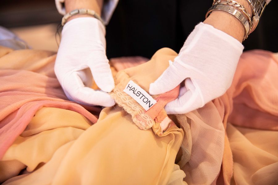 Gloves holding clothing tag titled "Halston" 