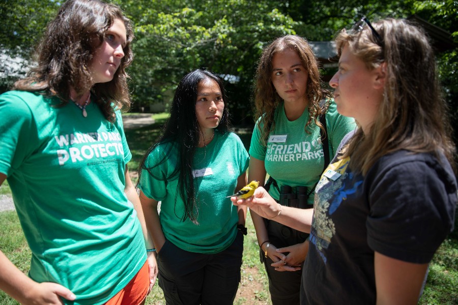 Interns speak with research team member who is holding a gold finch.