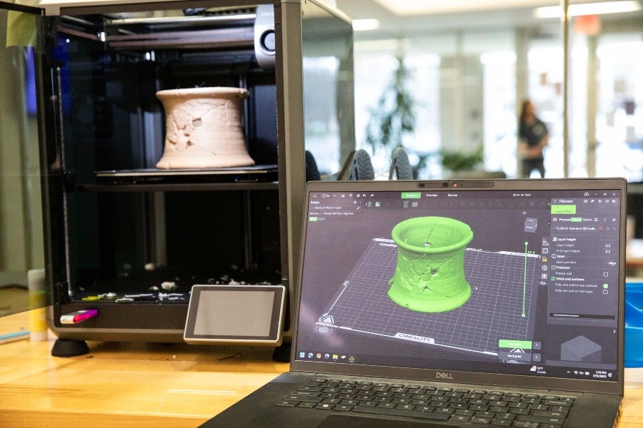 The replica jar holder in the 3-D printer and a computer showing the image of the jar holder that the 3-D printer works from.