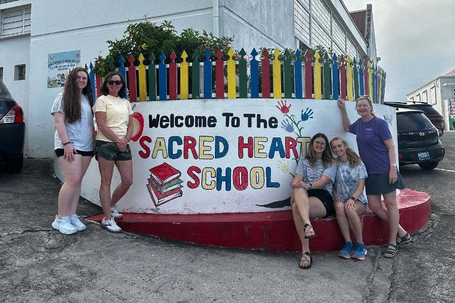 The school counseling student mission team posing with the Sacred Heart School sign