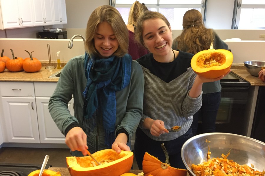 Two students scoop out pumpkin seeds.