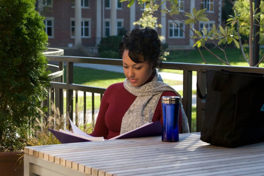 Female student sitting outside at table reading. 