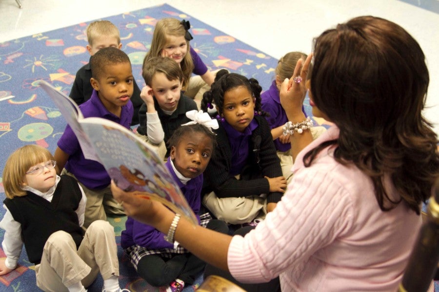 Teacher reads book to group of elementary school children.