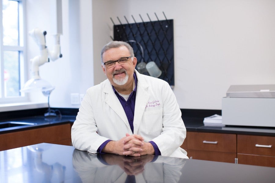 Kent Gallaher sitting in biology lab wearing white coat