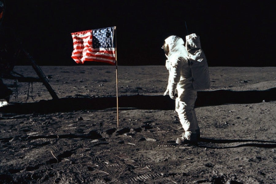 Neil Armstrong standing on moon near US flag.