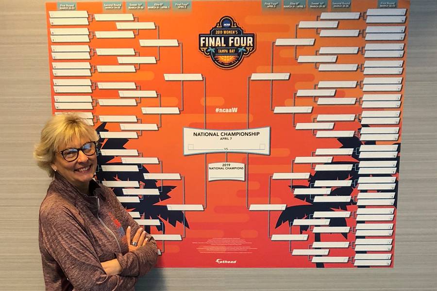 Diane Turnham standing next to NCAA women's basketball tournament brackets