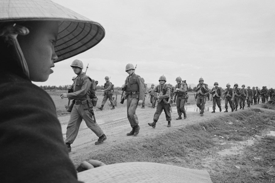 Photo from Vietnam War with soliders marching in a line in a field. 