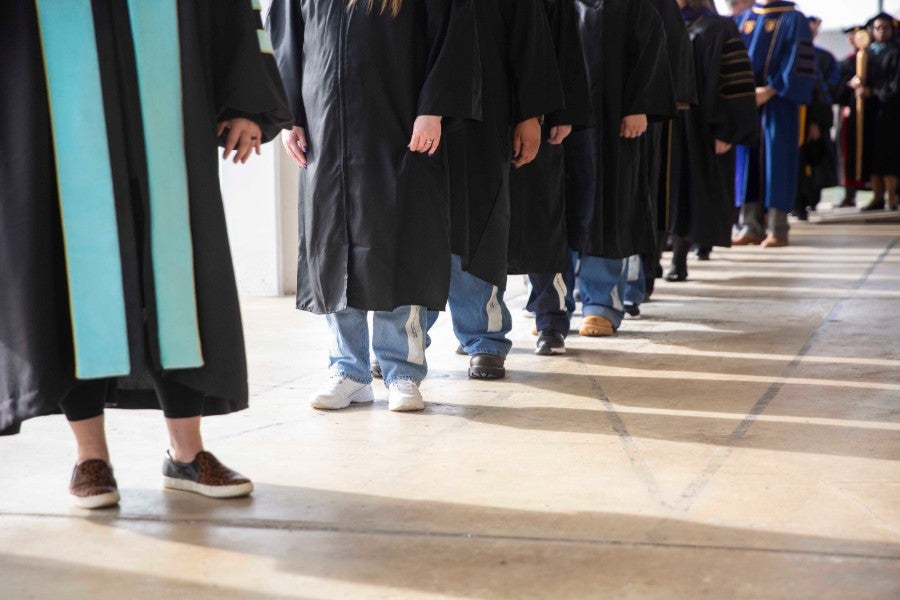Graduates wearing graduation robes over prison blues.
