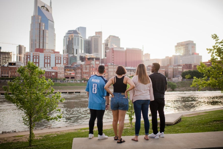 Tourists standing on riverfront looking at Nashville skyline.