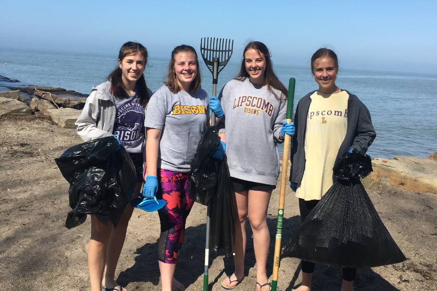 Four people standing together wearing Lipscomb shirts and holding rakes.